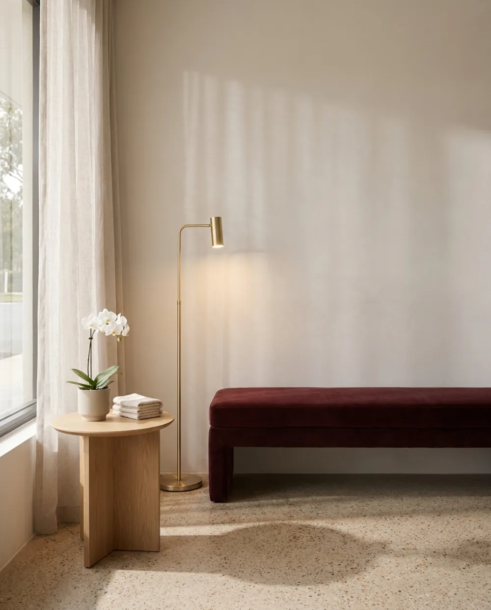 Empfangsbereich eines YASZEY® Beauty Studios: Sitzbank in Bordeaux, Stehleuchte in Champagnergold und eine Orchidee vor heller Wand